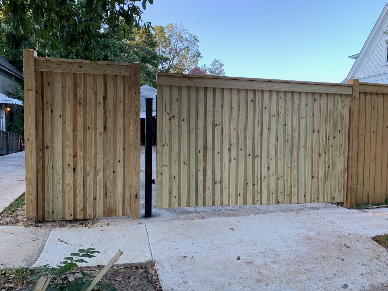 Wooden privacy fence with a gate beside a concrete driveway under a blue sky