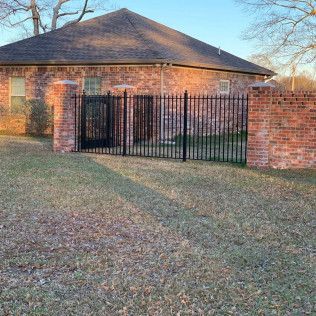 Brick house with a black metal gate and brick fence beside a grassy yard at sunset