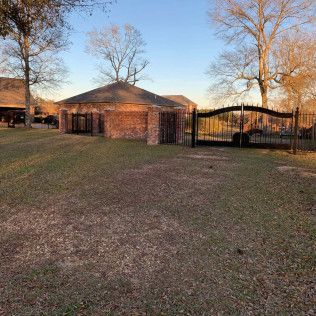 Brick house with a gated carport in a grassy yard at sunset