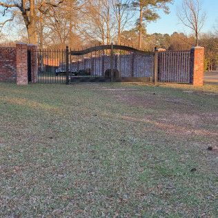 Brick gate and black iron fence enclosing a small stone building on a grassy lot at sunset