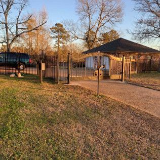 Small fenced park entrance with a gazebo, parked SUV, and trees in warm late-afternoon light