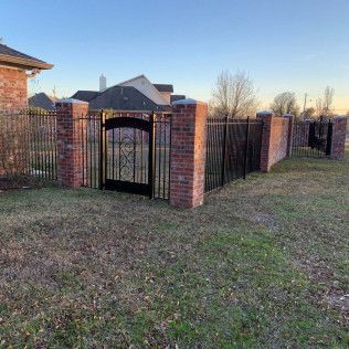 Brick fence and black metal gate beside a grassy yard at sunset.