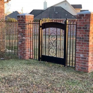 Black wrought-iron gate between red brick pillars in a suburban yard with a house in the background