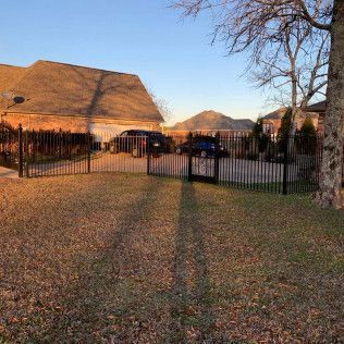 Fenced yard with autumn leaves, a house, parked cars, and long shadows at sunset.
