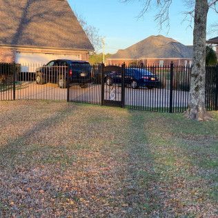 Residential driveway with black gate, parked cars, and thatched-roof buildings at sunset