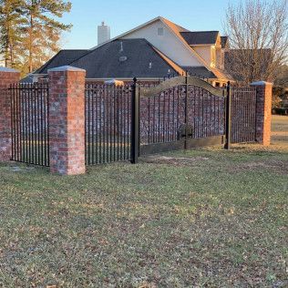 Brick-and-metal fence with black gate in front of a house on a grassy yard