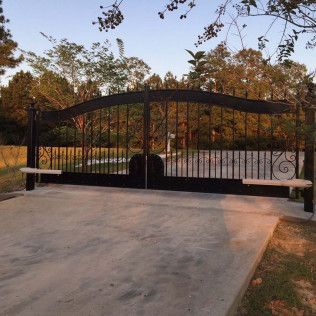 Closed black metal driveway gate across a concrete driveway at sunset