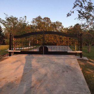 Black metal gate across a concrete driveway at sunset, with trees and bushes in the background