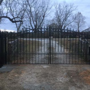 Black metal gate blocking a flooded driveway under leafless trees at dusk