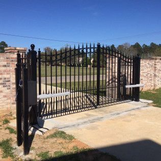 Black wrought-iron gate between brick walls at a park entrance on a sunny day