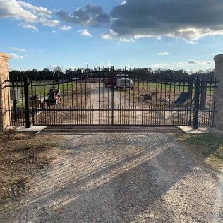 Closed black metal gate at the entrance to a gravel driveway under a partly cloudy sky