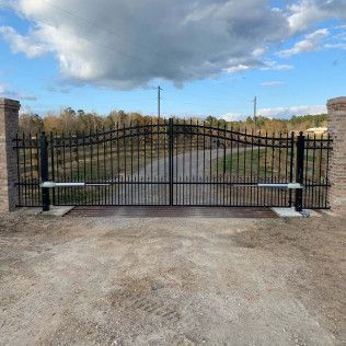 Black metal gate between stone pillars on a gravel driveway under a cloudy sky