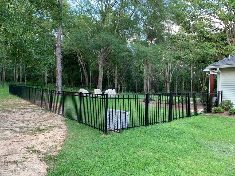 Black metal fence around grassy backyard with trees and a white house corner nearby