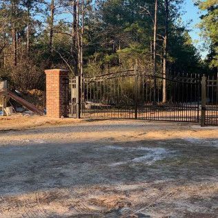 Black metal gate between brick pillars at a wooded driveway entrance