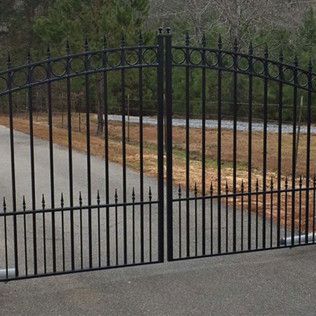 Black wrought-iron gate across a driveway, with a stone wall and trees in the background