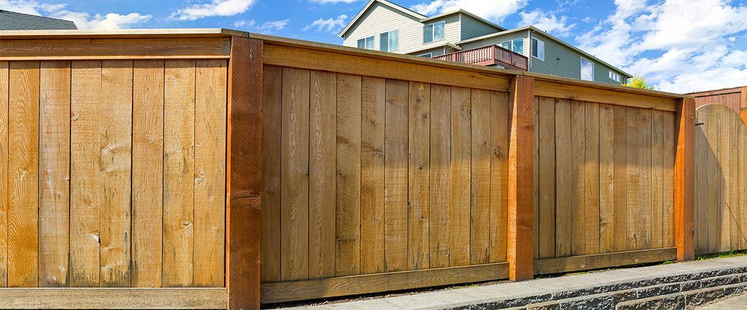 Wooden privacy fence along a street, with houses visible above it