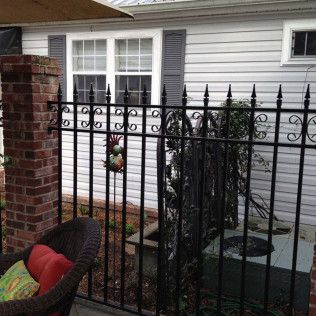 Black metal fence in front of a white house with brick pillar and small hanging ornament