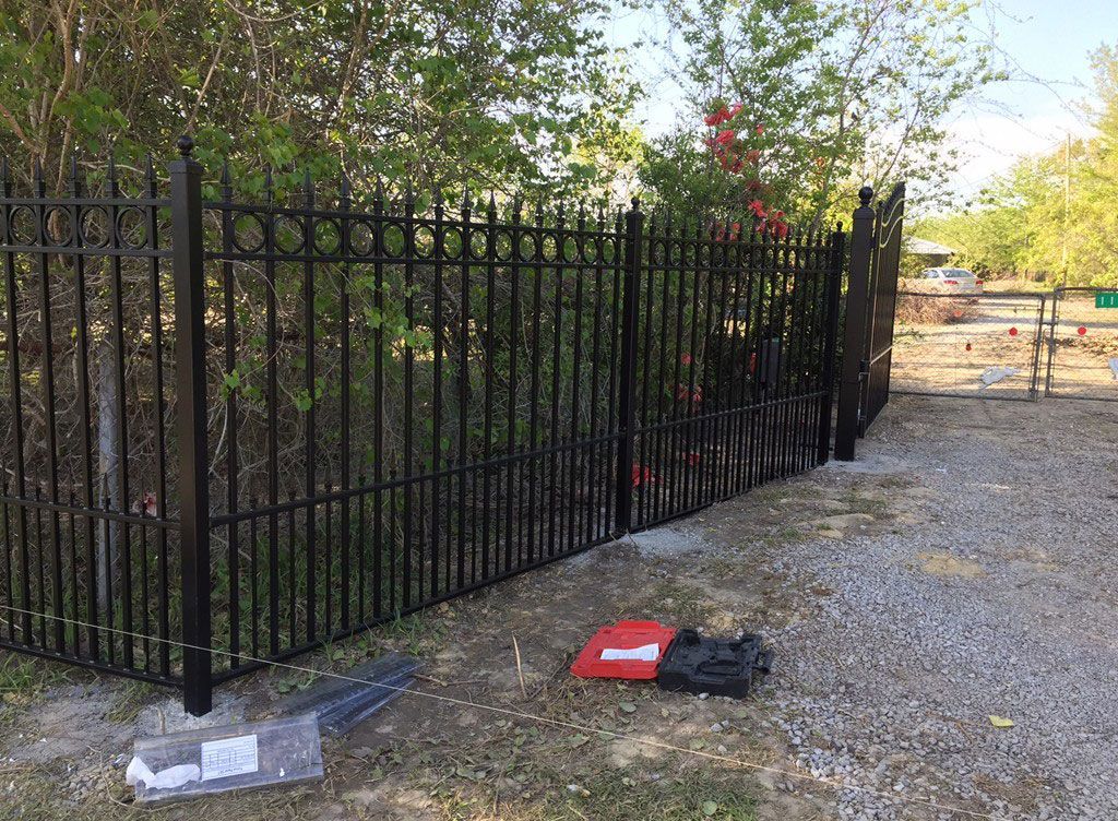 Black metal fence beside a gravel path with fallen items on the ground and trees behind it