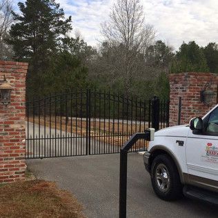 Black iron driveway gate between brick pillars with a white utility truck parked at right.