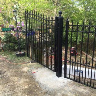 Black wrought-iron gate and fence beside a garden path with greenery and flowers