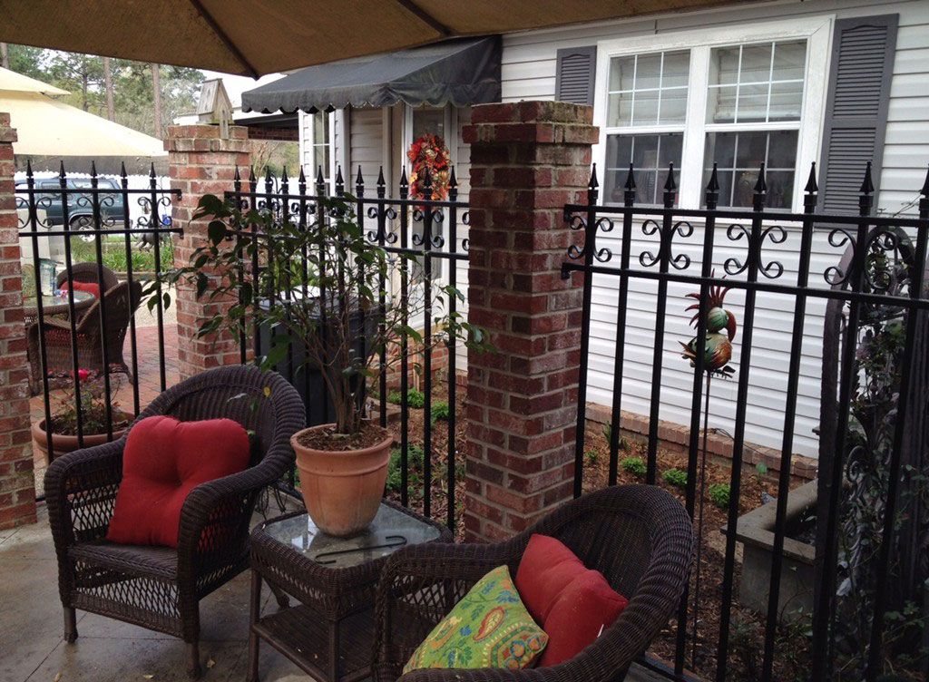Patio seating with red cushions beside a brick house and black iron fence under a canopy