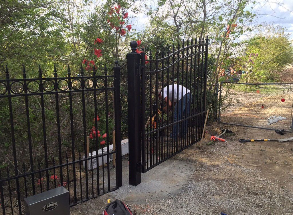 Person in white shirt crouching by a black iron fence in a garden area.