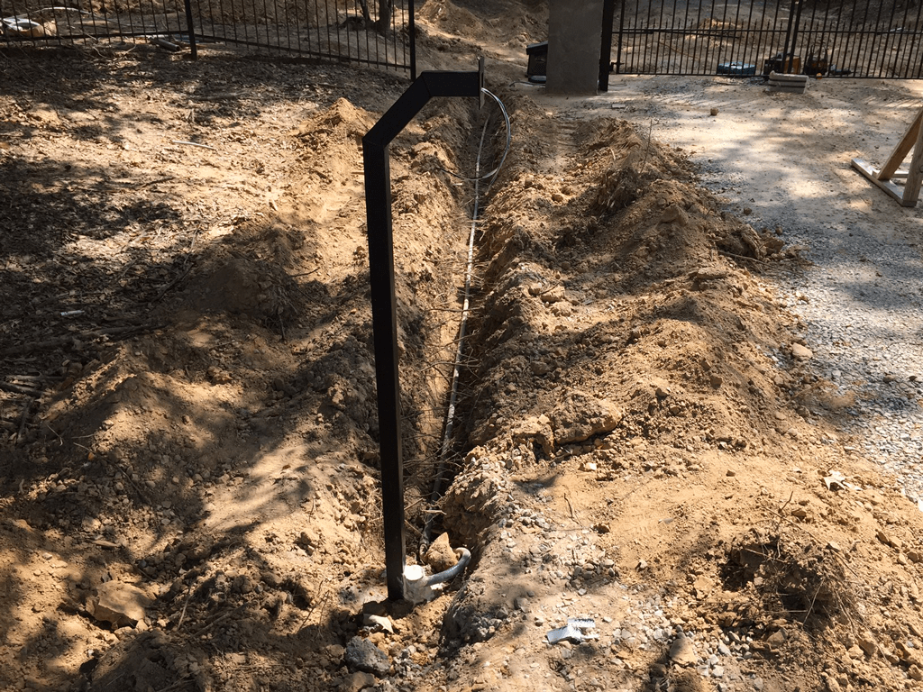 Black metal post in a dirt trench at a construction site with wooden fencing and trees nearby