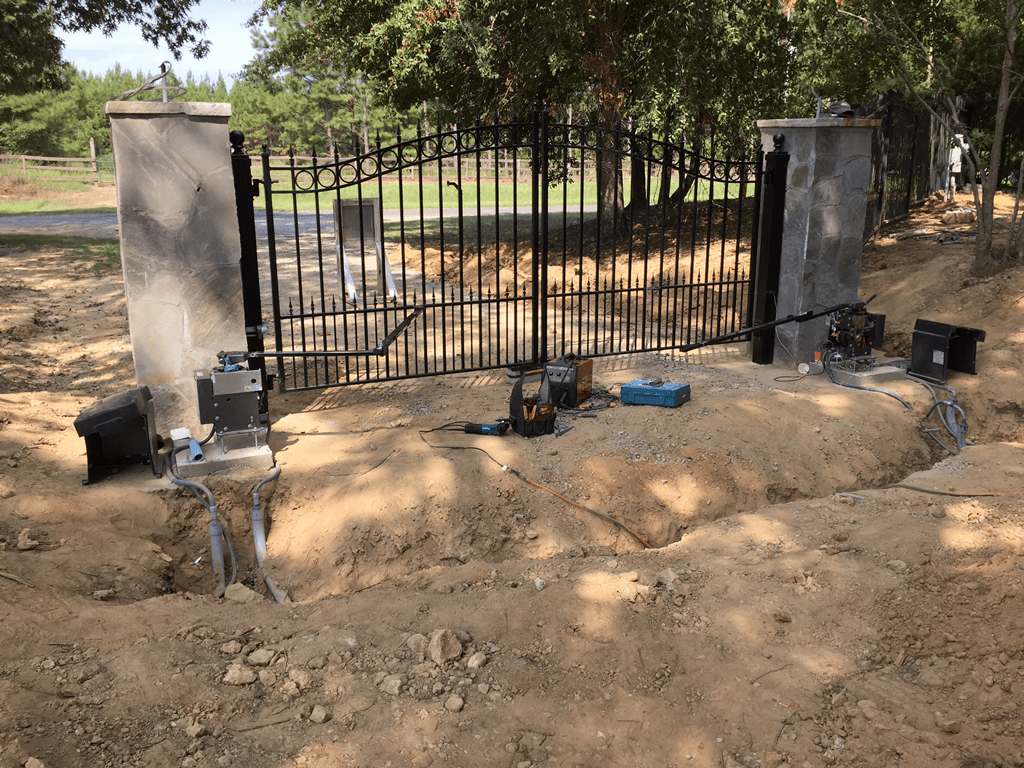 Black metal gate between concrete pillars on a dirt road in a wooded area