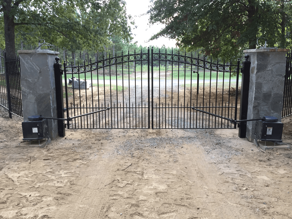 Closed black iron gate between stone pillars at a sandy driveway entrance