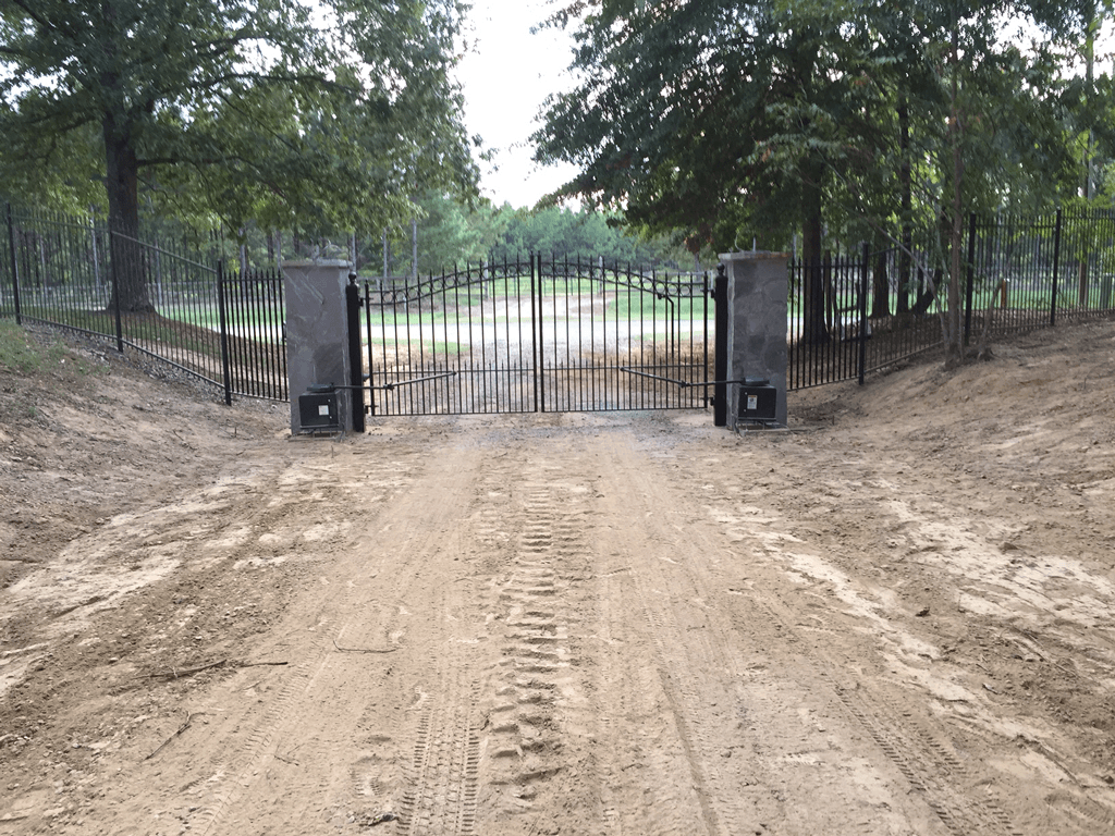 Dirt road leading to a closed metal gate between trees and stone pillars