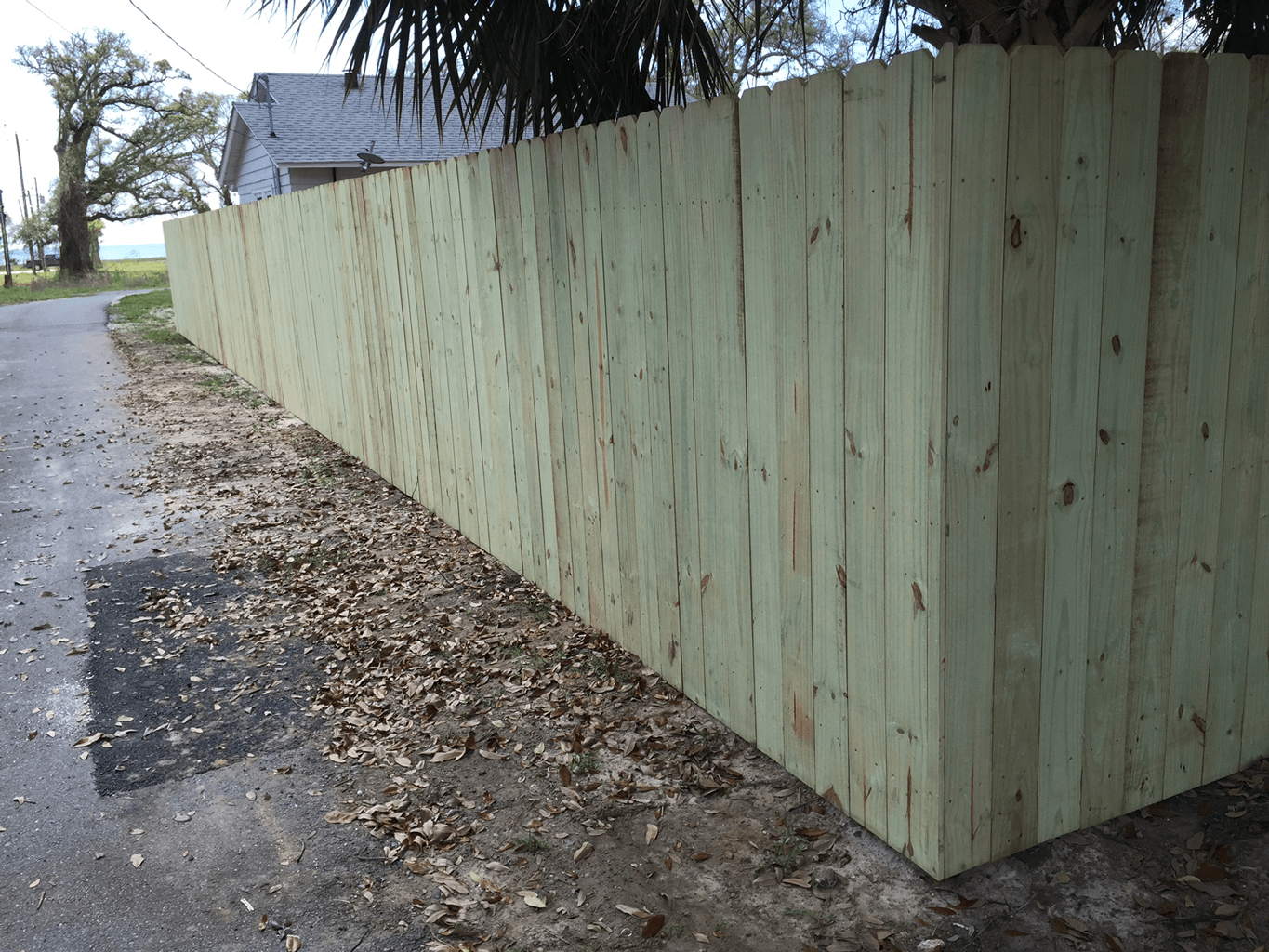 Long pale-green wooden fence along a wet roadside on a cloudy day