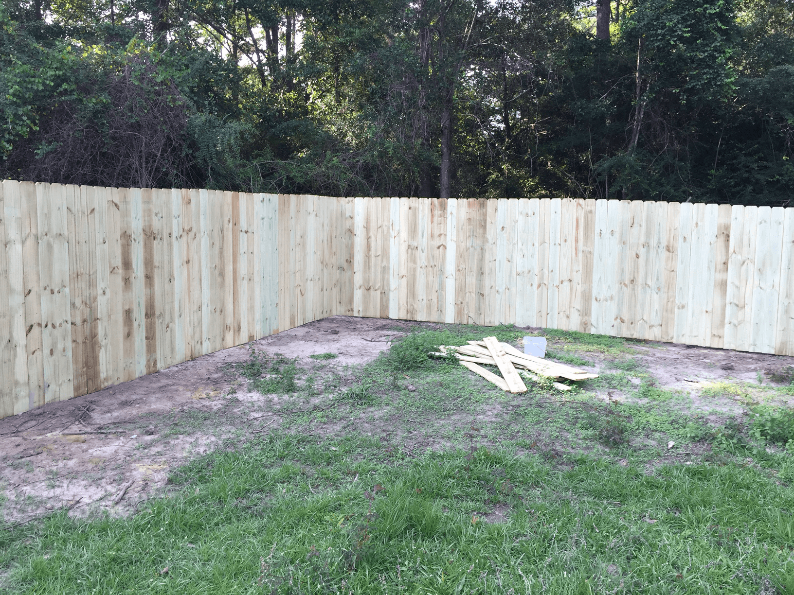 Empty fenced backyard with a new wooden privacy fence and patches of dirt and grass.