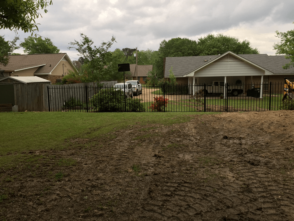 Backyard with patchy grass, a fenced yard, and houses under cloudy skies