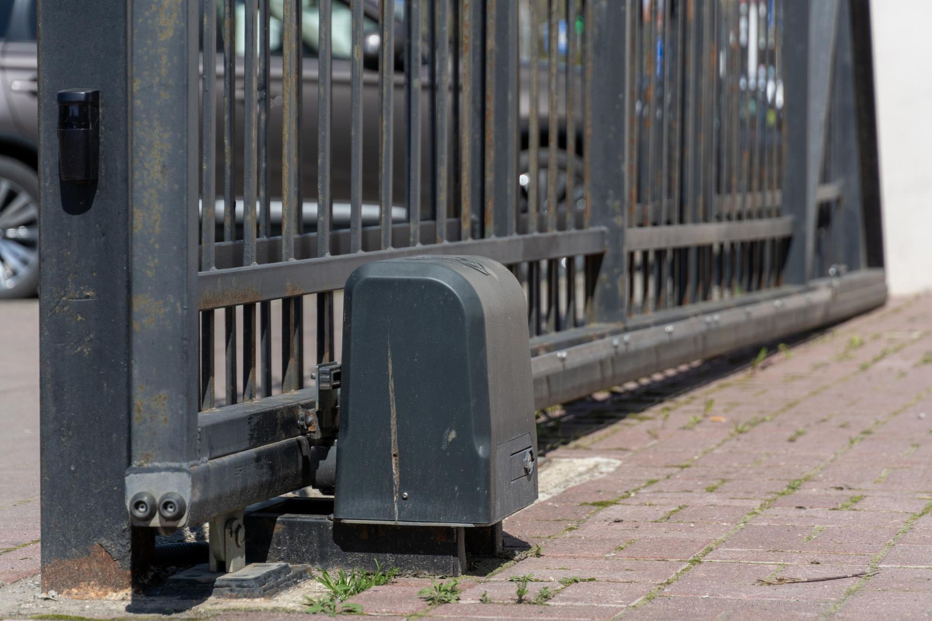 Automated sliding gate with gray motor housing beside a brick sidewalk and metal fence