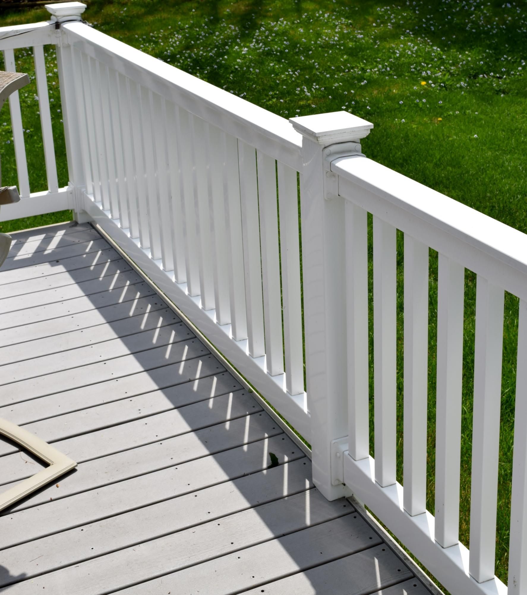 White deck railing beside a gray wooden deck, overlooking a green lawn in sunlight