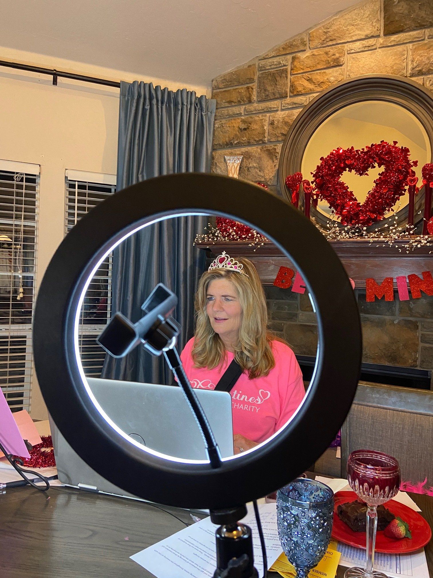 A woman is sitting at a table with a laptop and a ring light.