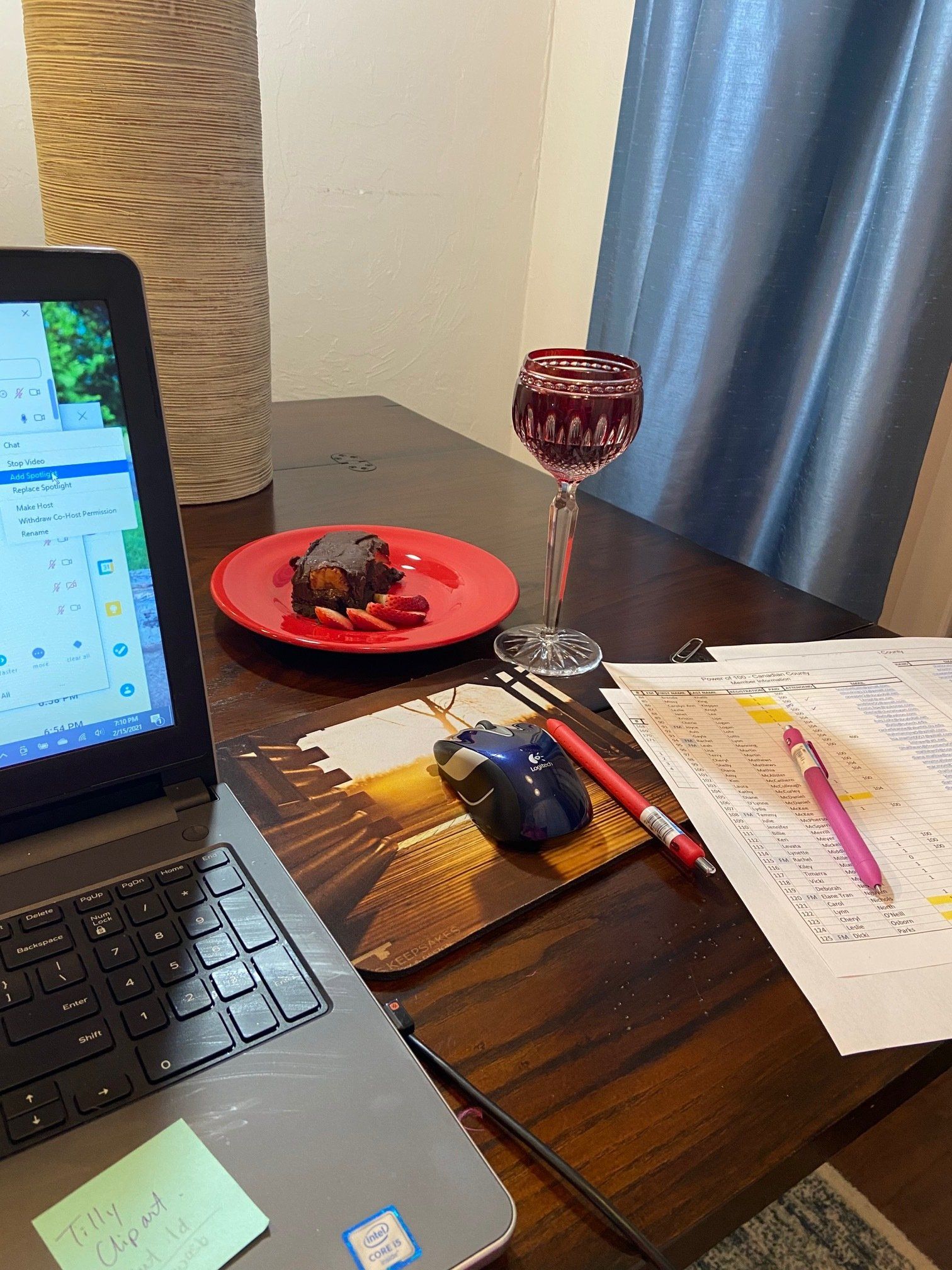 A laptop computer is sitting on a wooden table next to a plate of food and a glass of wine.