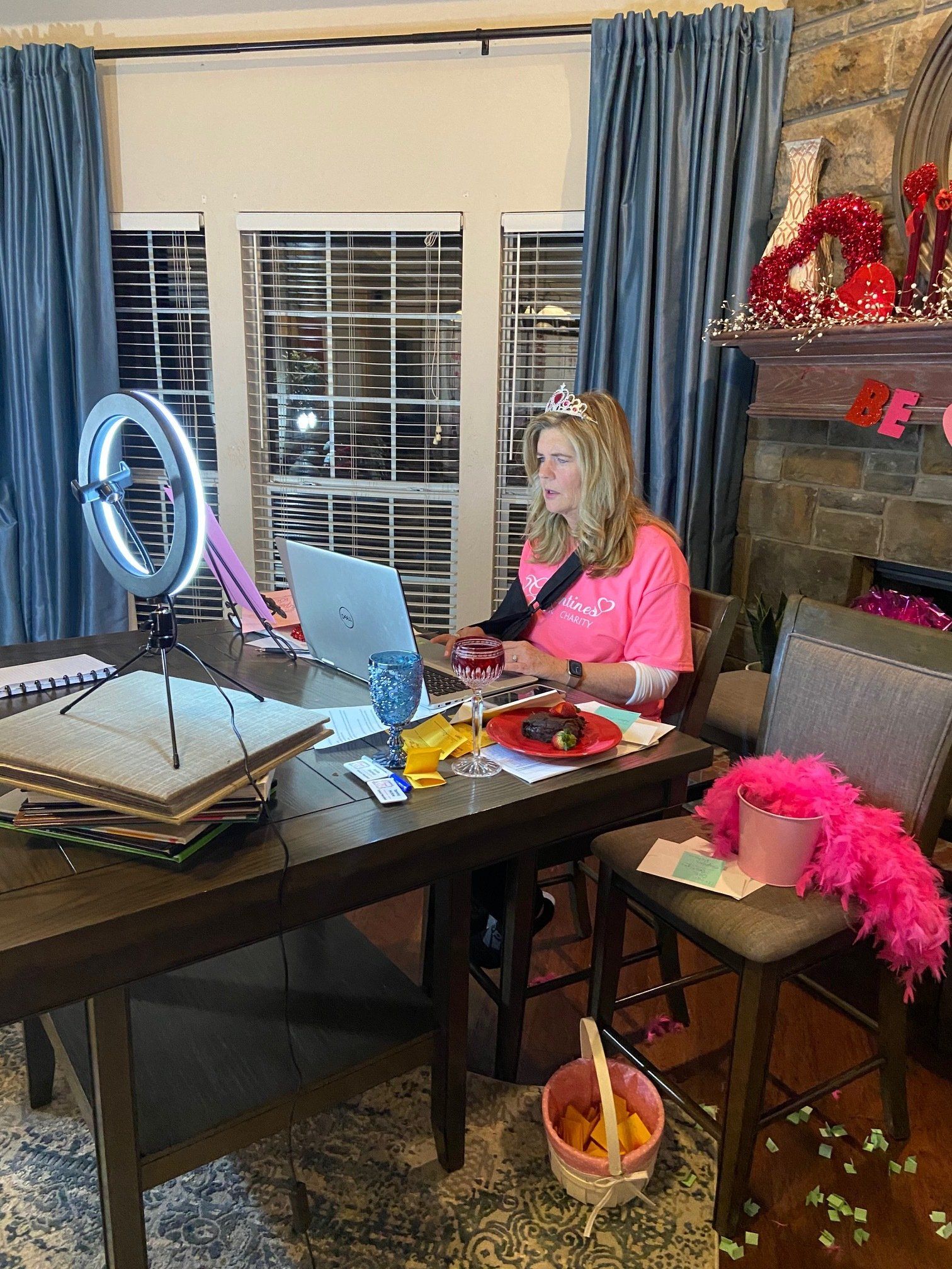 A woman is sitting at a table with a laptop and a ring light.