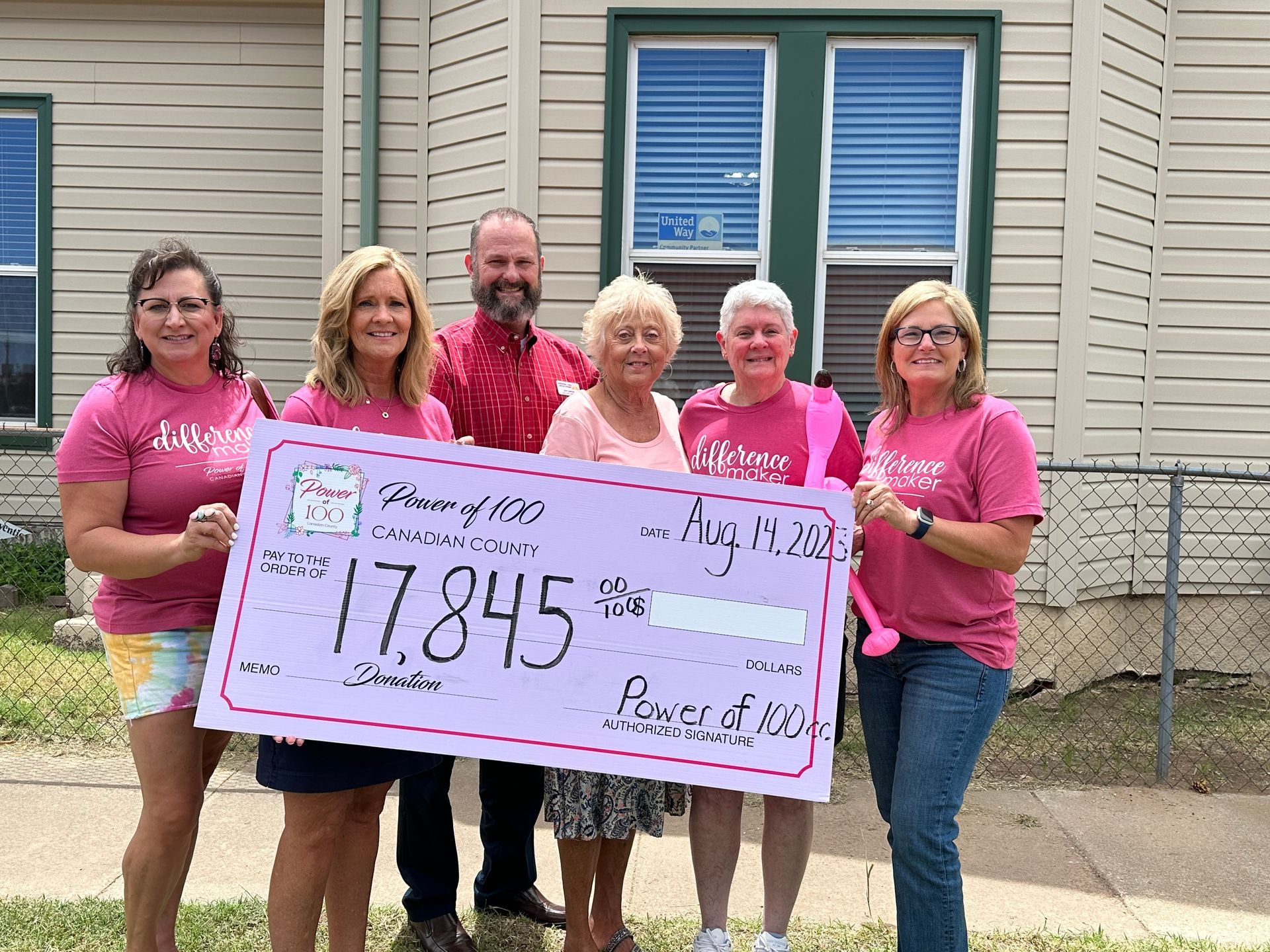 A group of people are holding a check in front of a house.