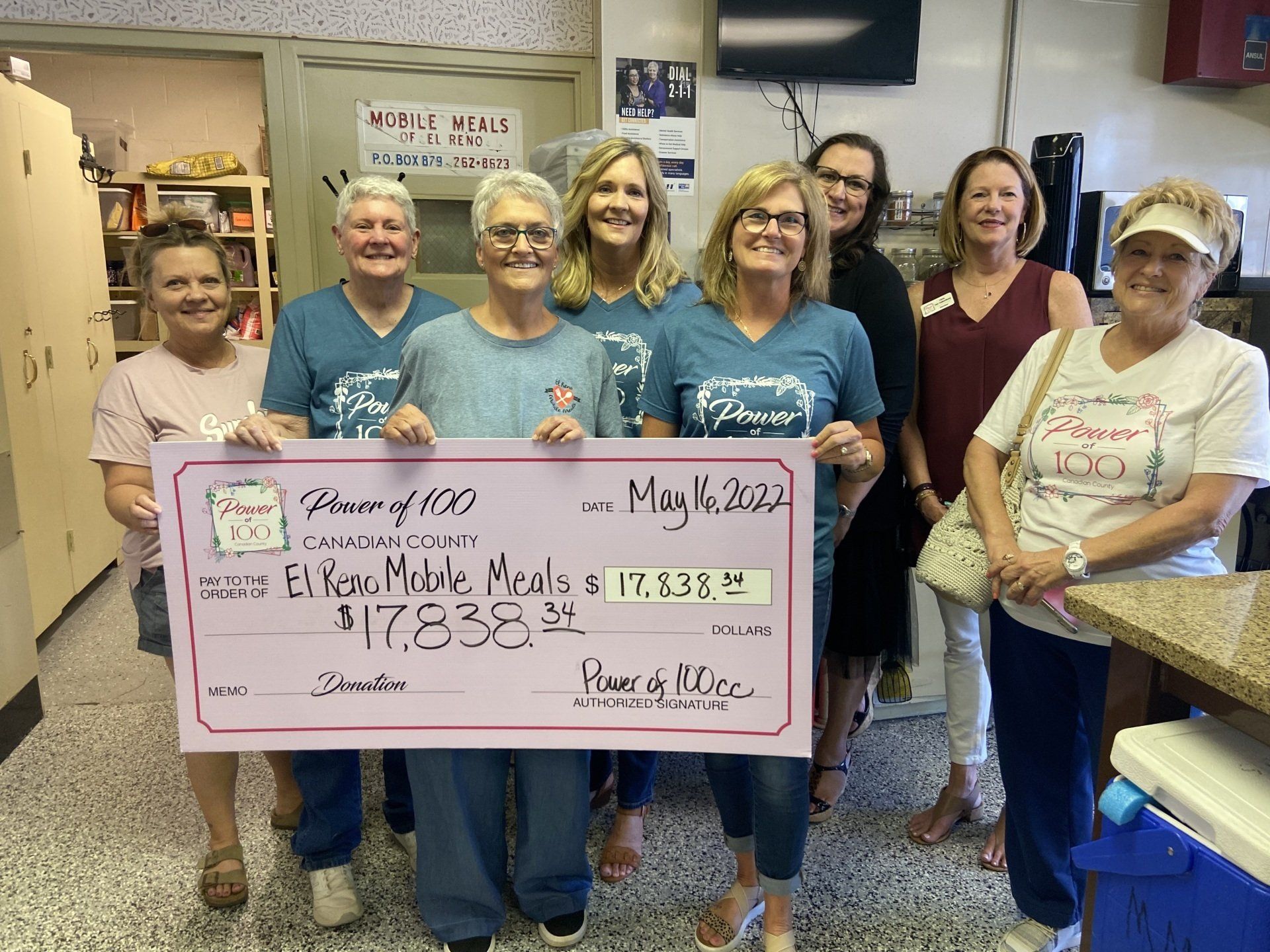 A group of people are holding a large check in a kitchen.