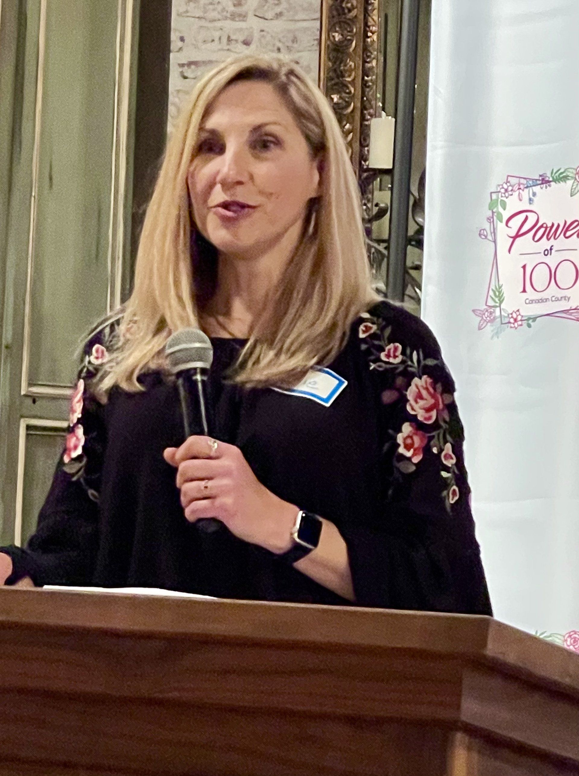 A woman is standing at a podium holding a microphone.