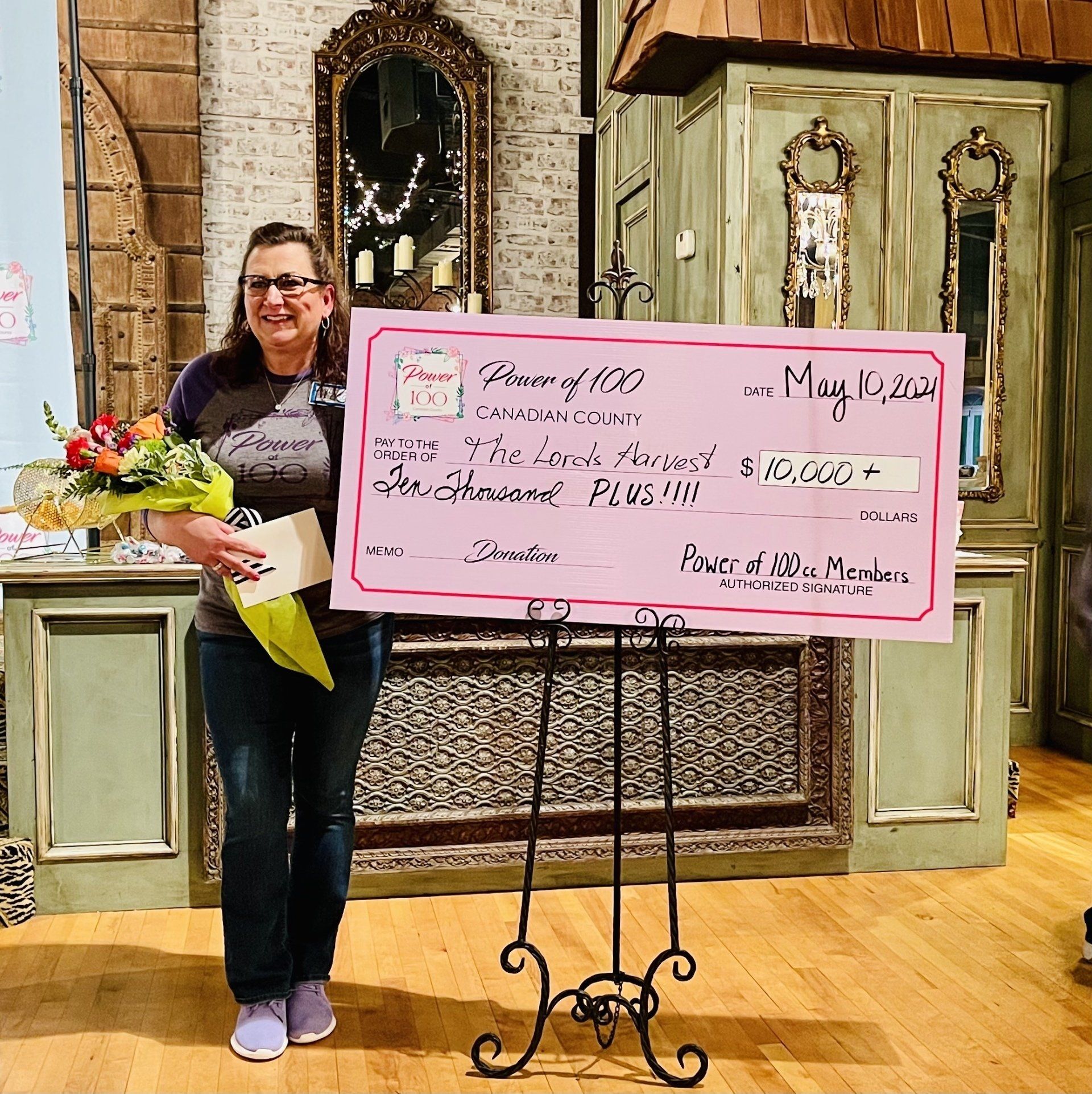A woman holding a bouquet of flowers stands in front of a check that says power of 100