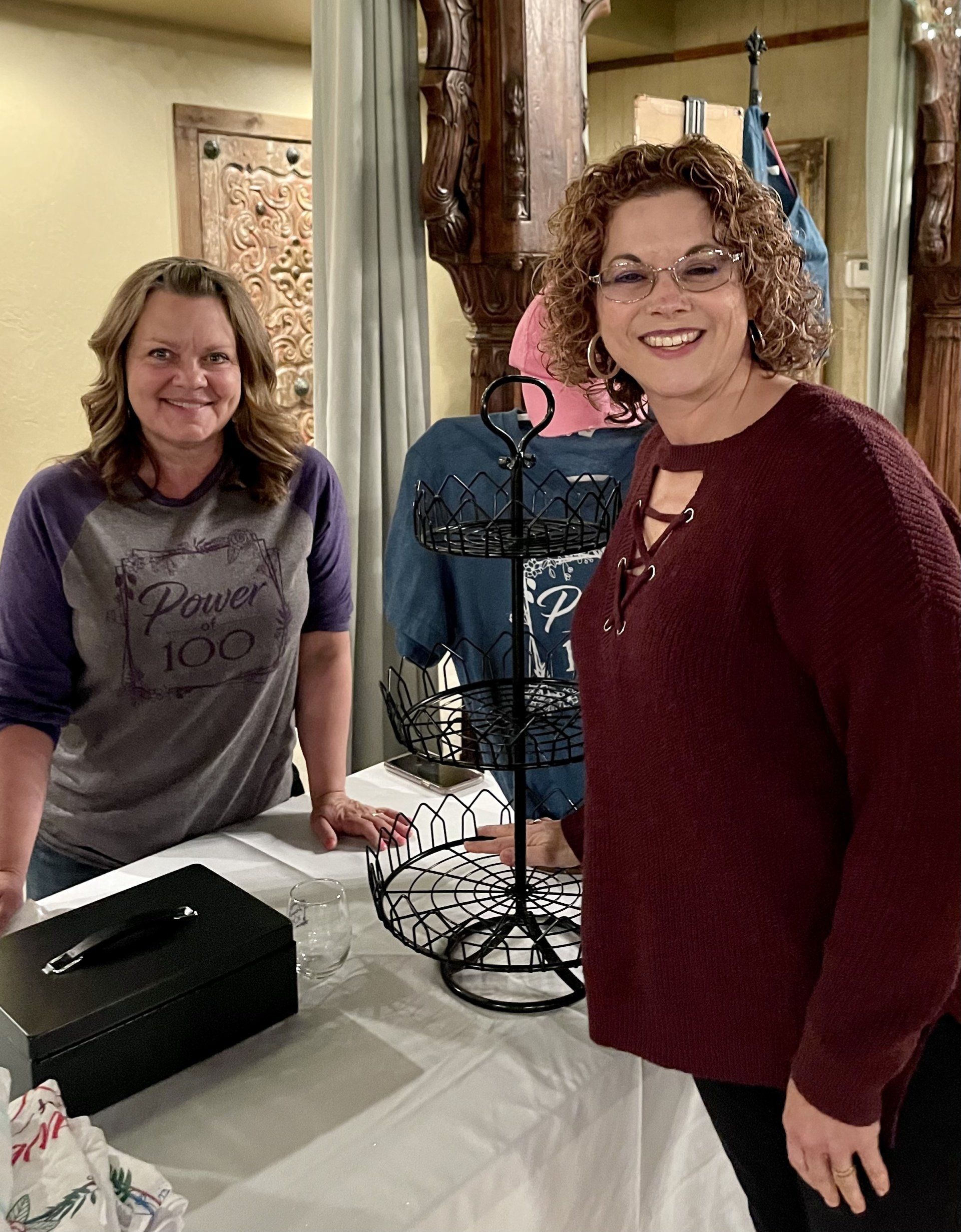 Two women are standing next to each other in front of a table.
