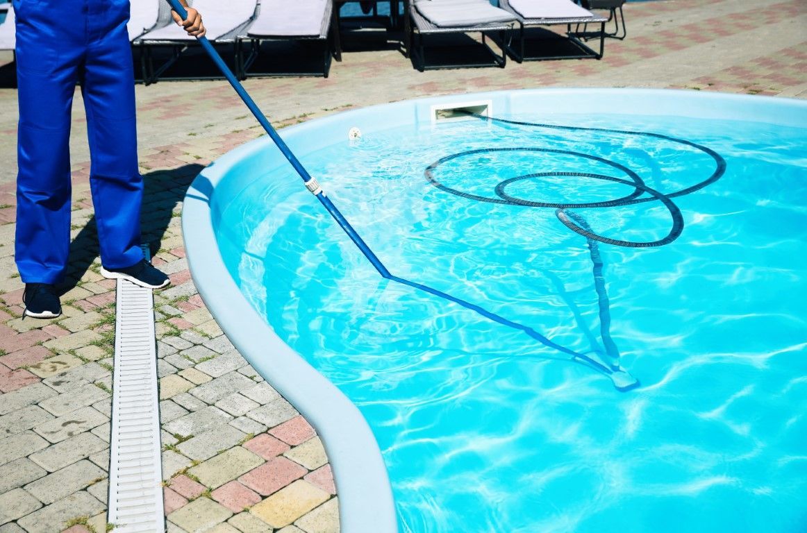 Person cleaning a blue swimming pool with a net and hose.