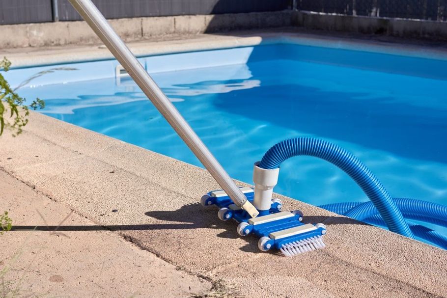 Pool vacuum cleaning a blue swimming pool. Blue and white brush head, blue hose, and white pole.