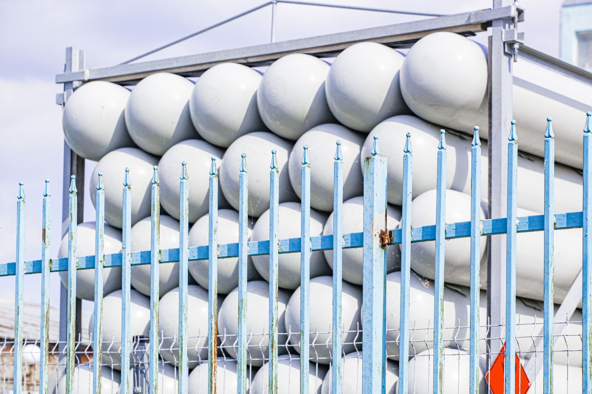 An image of rows of white propane gas cylinders stacked on top of each other behind a fence. An image of rows of white propane gas cylinders stacked on top of each other behind a fence.