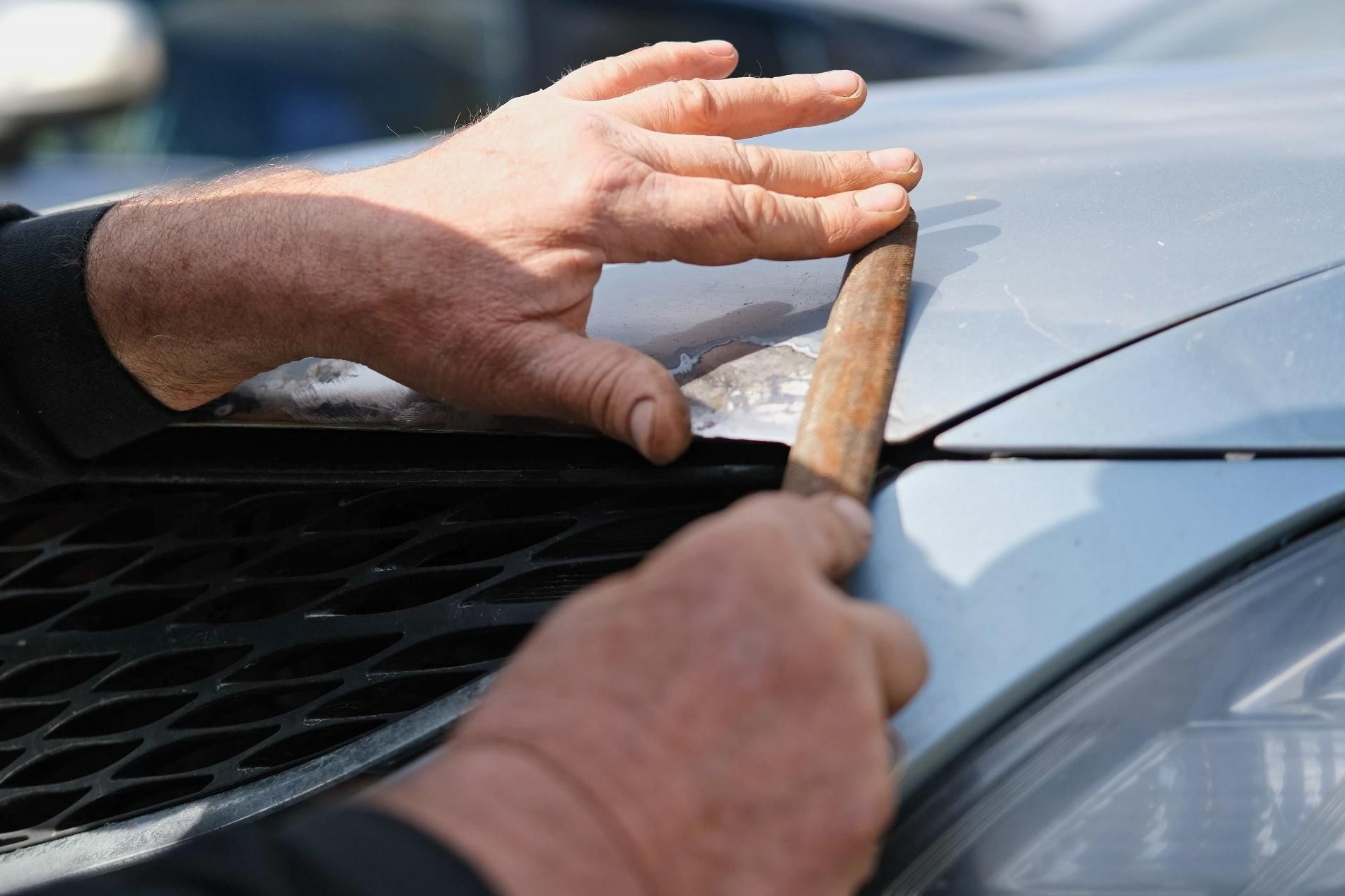 A Man Is Holding A Piece Of Wood Over The Hood Of A Car — Lyons Street Paint Panel in Bungalow, QLD