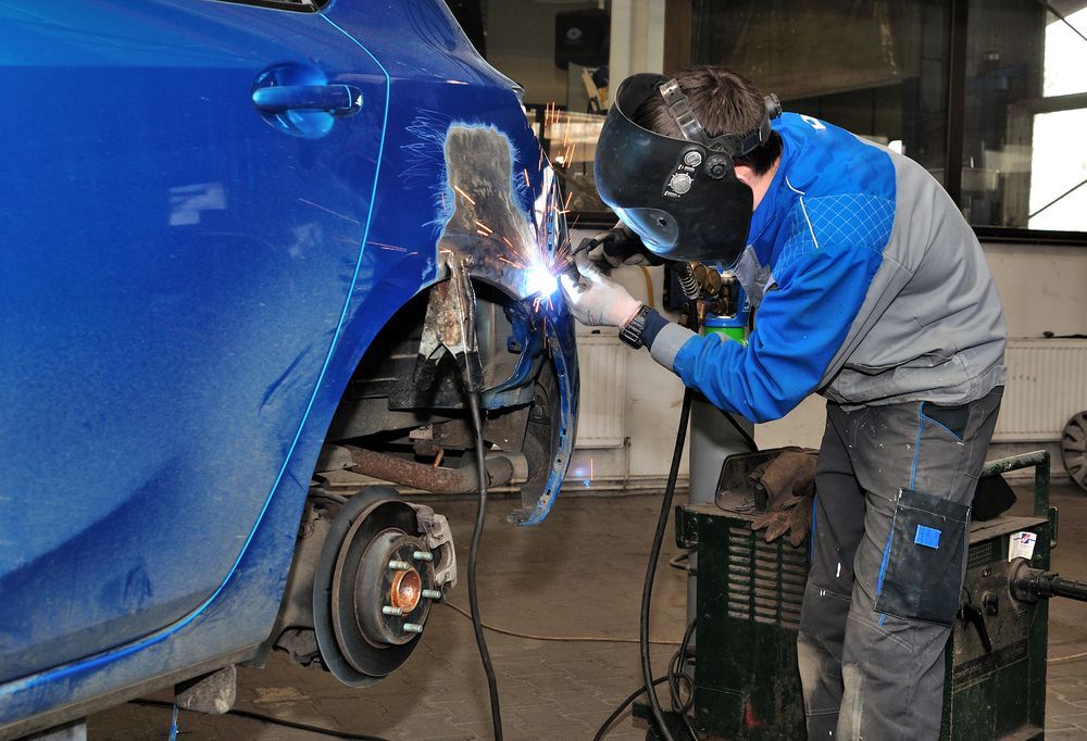 A Man Is Welding A Blue Car In A Garage — Lyons Street Paint Panel in Bungalow, QLD