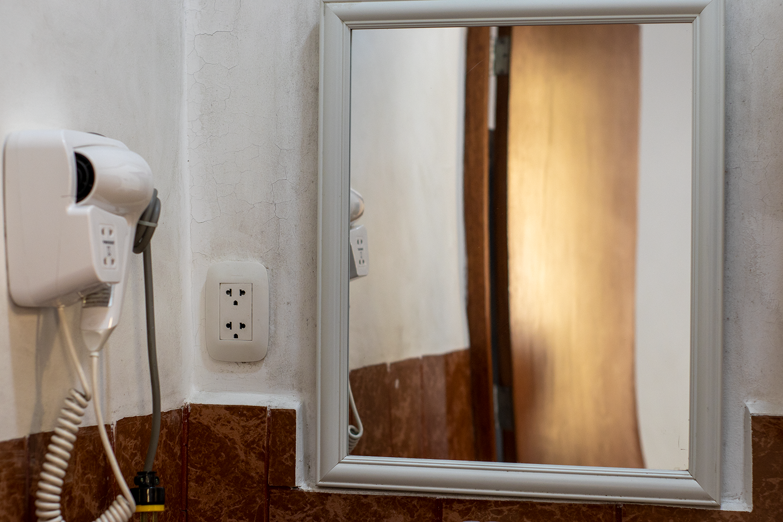 White hairdryer and electrical outlet next to a framed mirror in a bathroom.