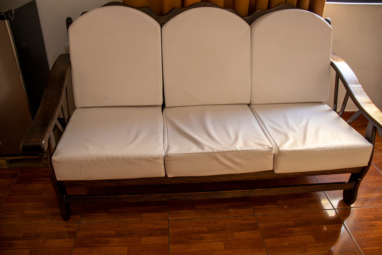 Three-seat wooden sofa with white cushions on a brown tiled floor.